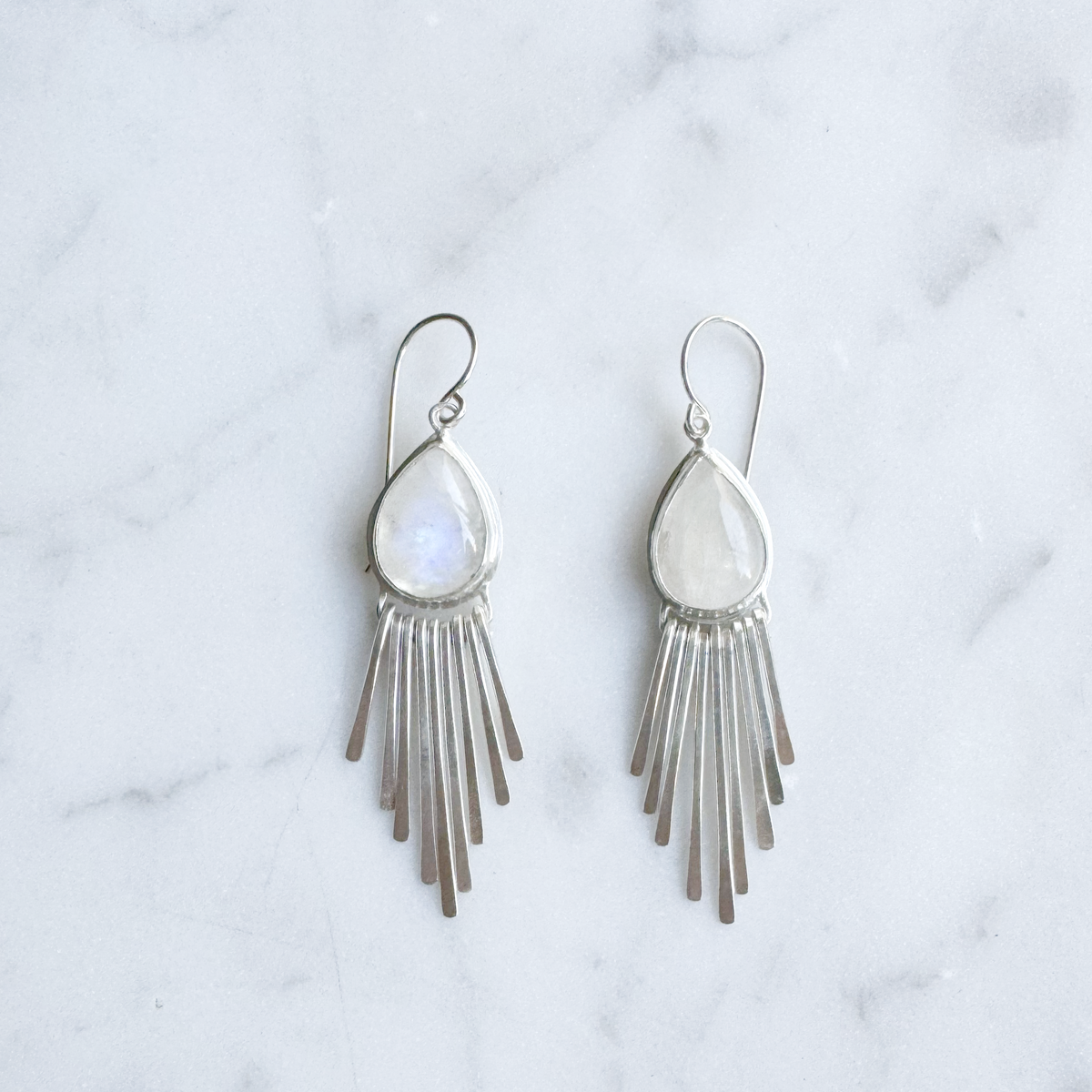 Silver fringe earrings with teardrop moonstones on a marble surface