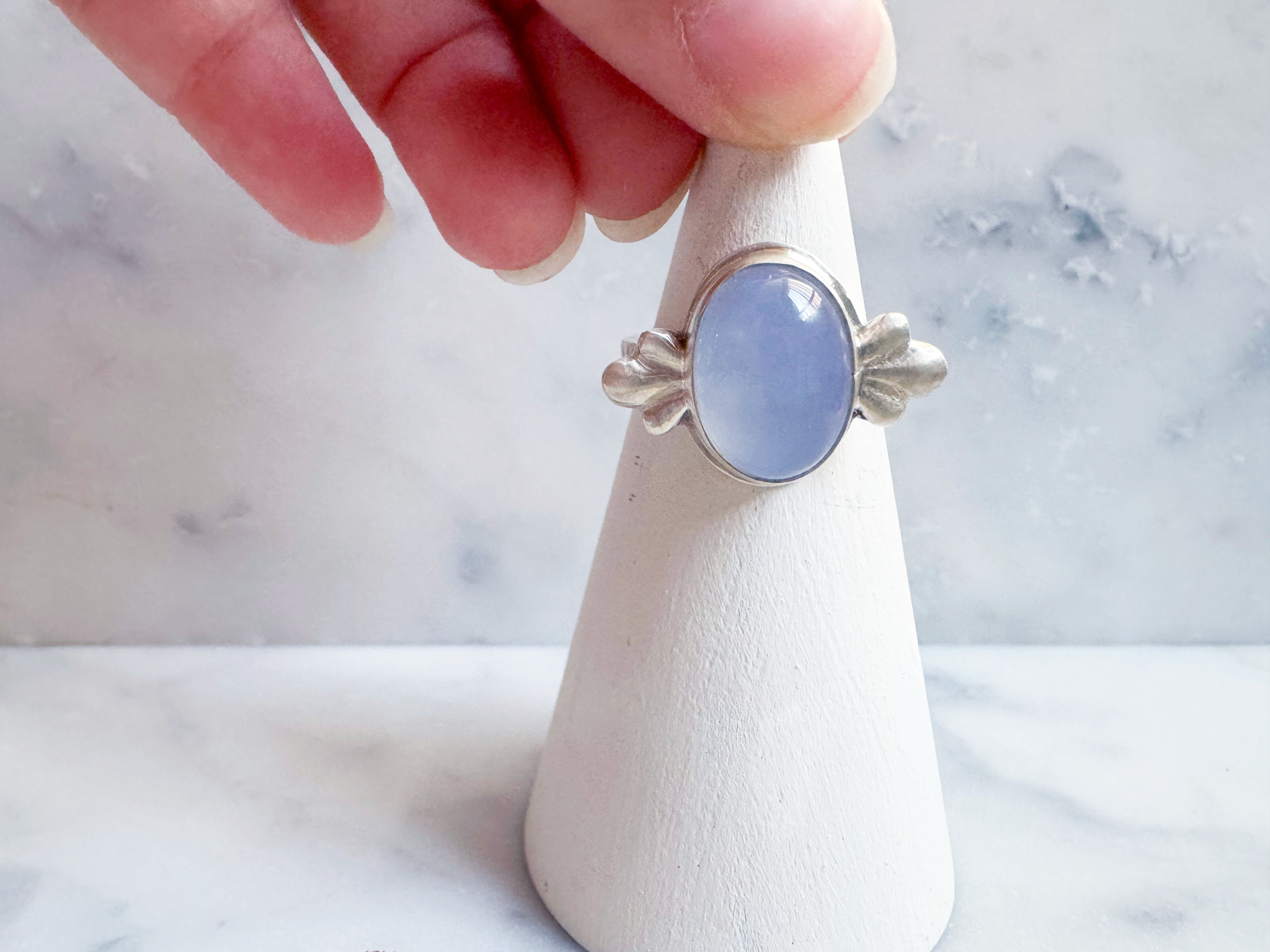 Silver ring with an oval blue stone on a white stand against a marble background