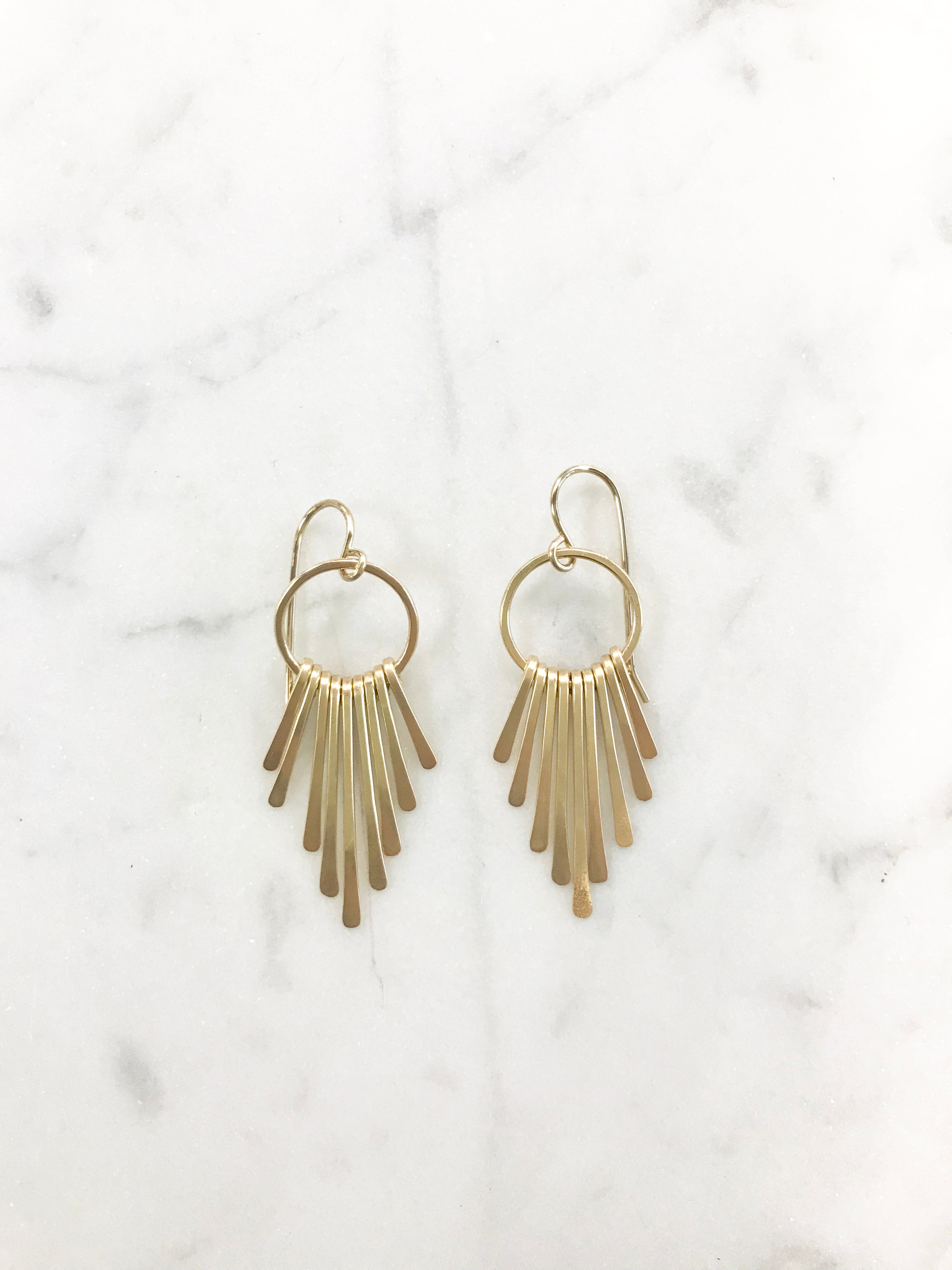 Small circle gold fringe earrings on a white marble background