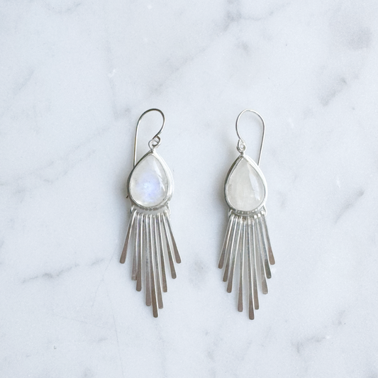 Silver fringe earrings with teardrop moonstones on a marble surface