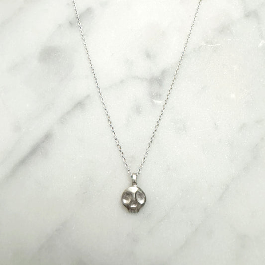 Silver necklace with a skull pendant on a white marble surface